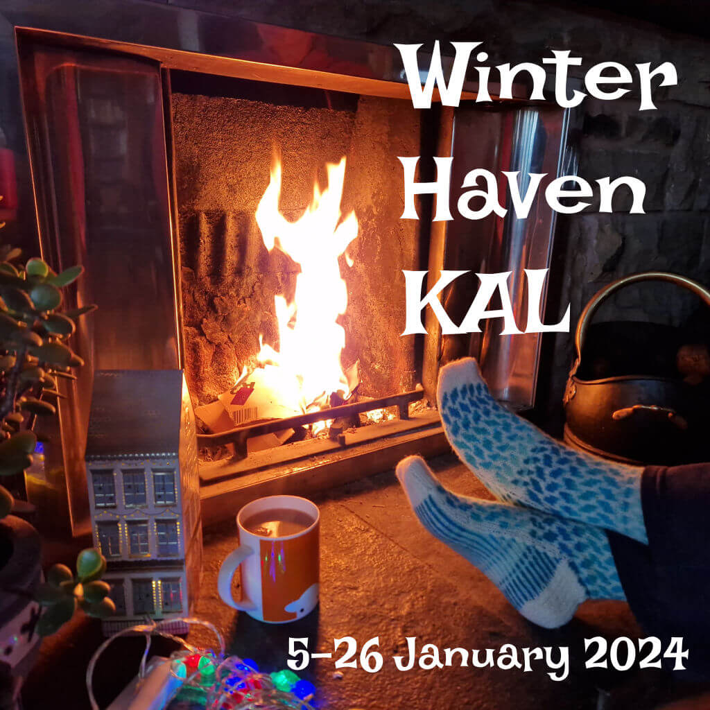 A pair of blue and white colourwork socks modelled on feet resting on a stone hearth in front of an open fire