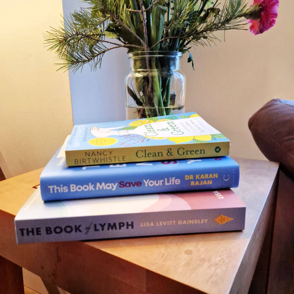 A pile of three books on a coffee table next to a vase of flowers