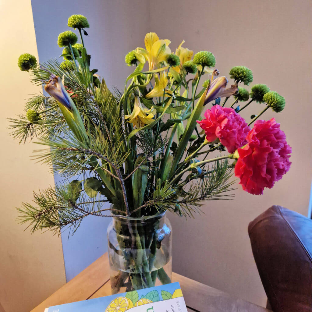 A vase of cut flowers in colours of pink, yellow and green on a coffee table