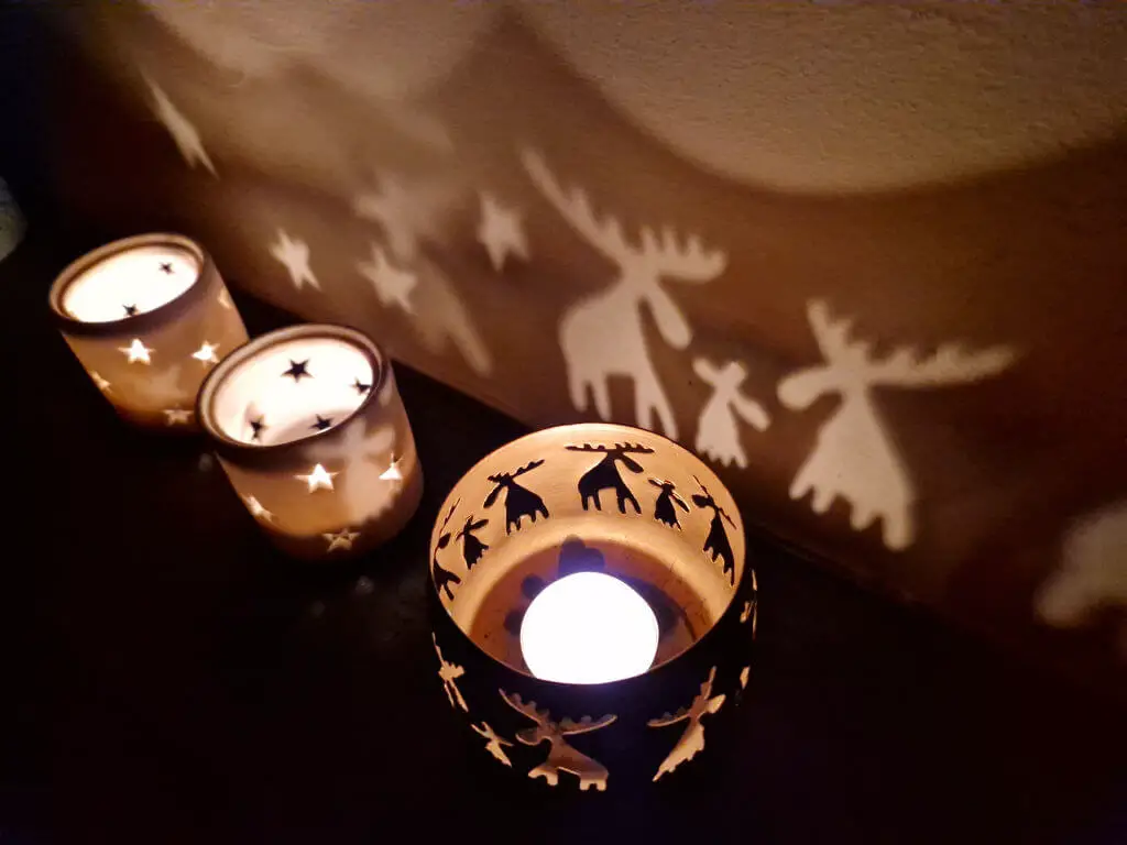 Three tea light holders throw light onto a wall. Two are star shaped and the third is a moose family