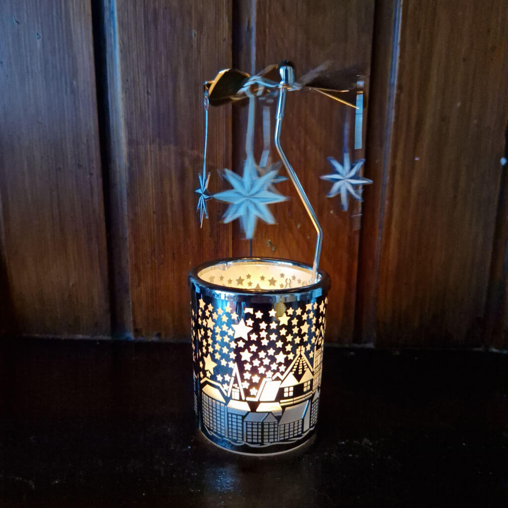 A tealight holder with a winter scene embossed on it. Above the candle is a spinning wheel with stars