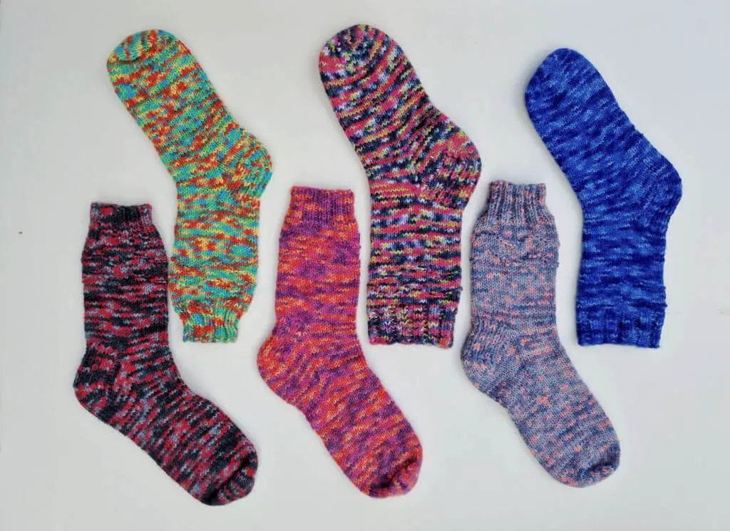 Six ColourLab Sock yarn socks in different colours arranged in a line so that the legs are together but the toes point up or down depending on where they are in the line