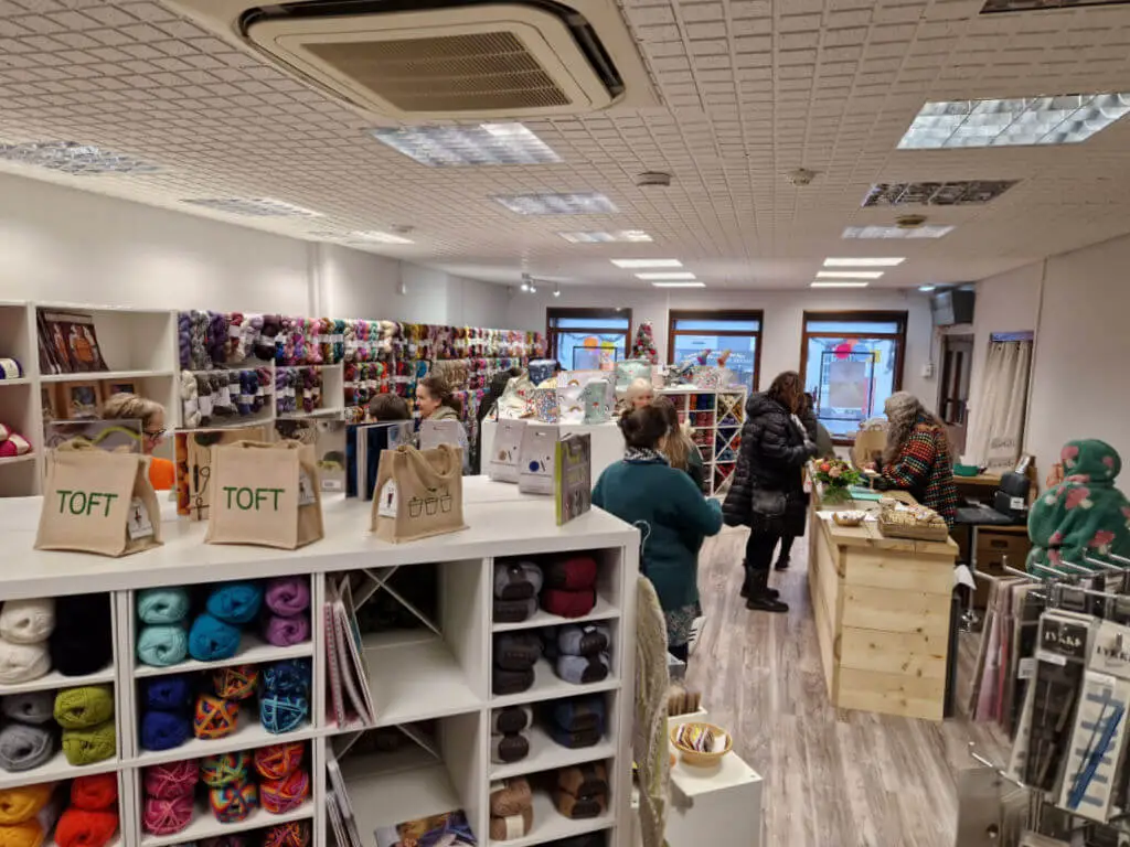 A view across a shop filled with display stands of yarn taken from the back of the shop