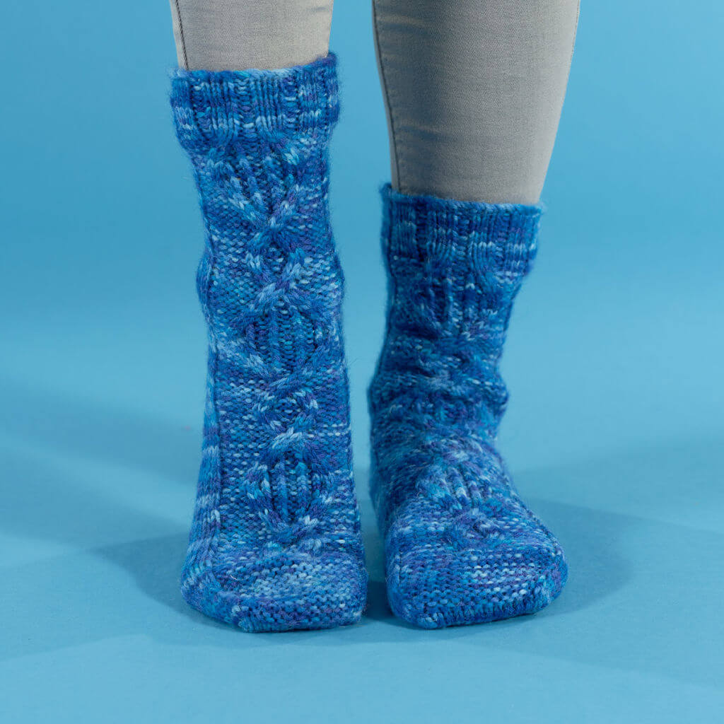 A pair of blue socks modelled on feet to show the cable detail to the front of the sock