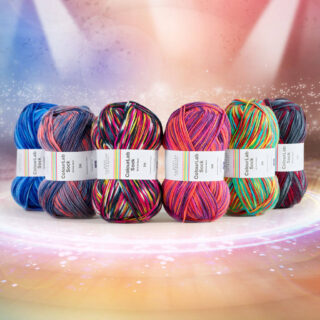 Six balls of coloured sock yarn lined up as if on a stage under spotlights