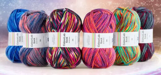 Six balls of coloured sock yarn lined up as if on a stage under spotlights
