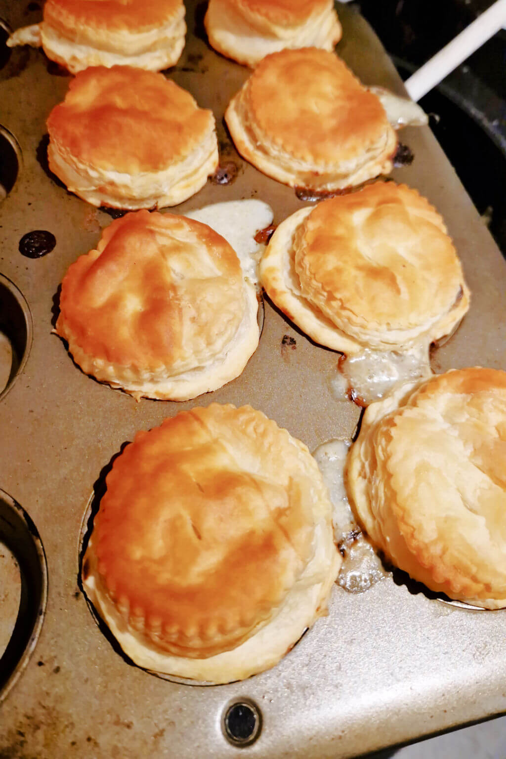 Eight golden pastry-topped pies in a muffin tin