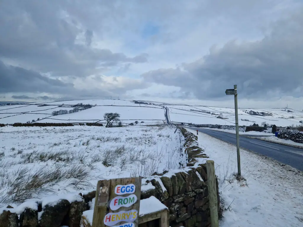 A view across snowy moorlands. In the foreground is an honesty box for eggs