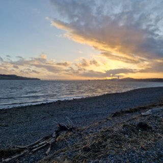 A view across a pebbly beach to a sunset in the distance