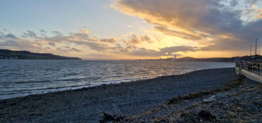 A view across a pebbly beach to a sunset in the distance