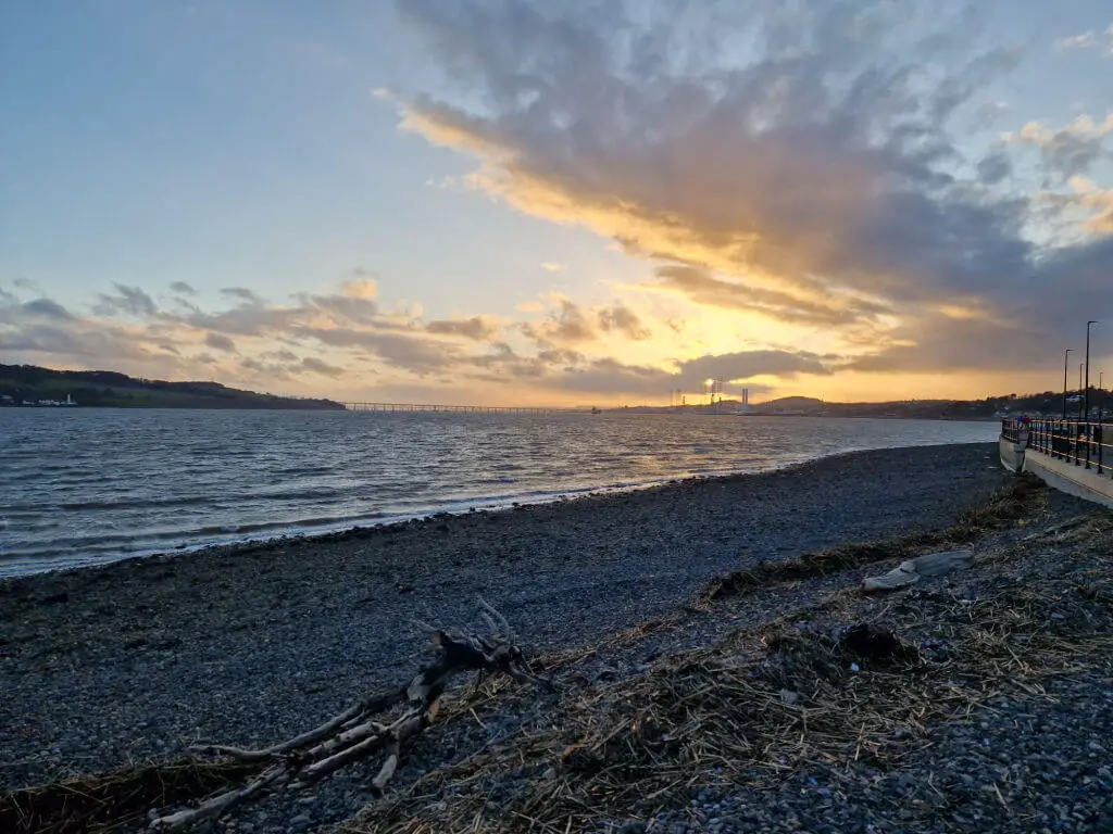 A view across a pebbly beach to a sunset in the distance