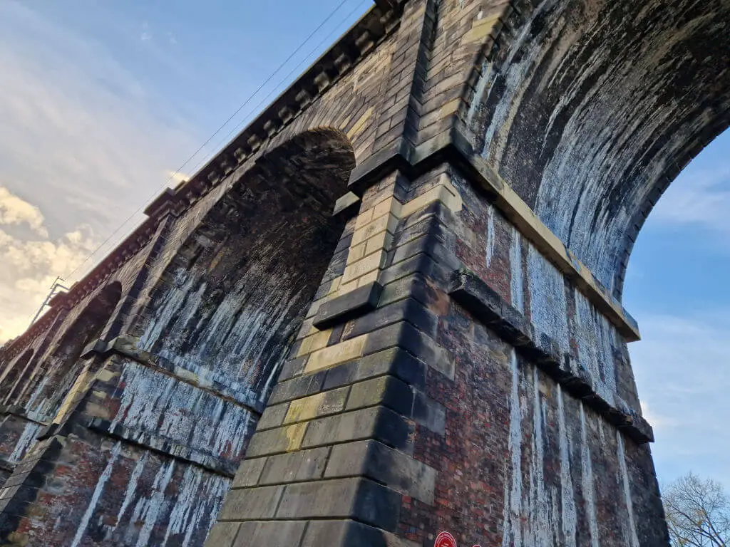 An upwards view of a stone railway viaduct showing lighter stone where the viaduct has been repaired