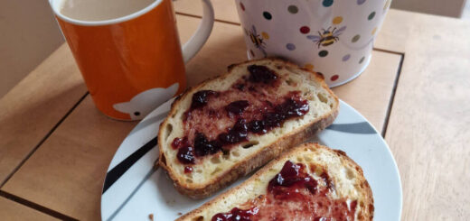 A wooden coffee table with a plant in a spotty plant pot, an orange mug of tea and two slices of toast and jam on a plate