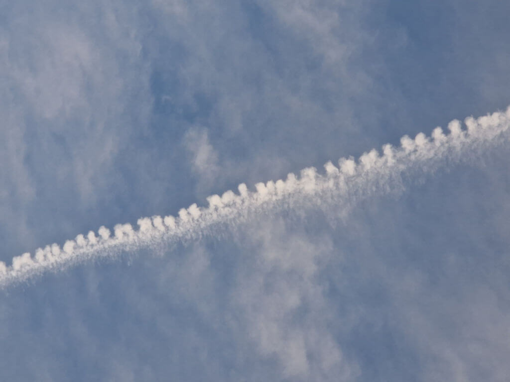 An aeroplane vapour trail in a cloudy sky. The vapour trail looks like a zip