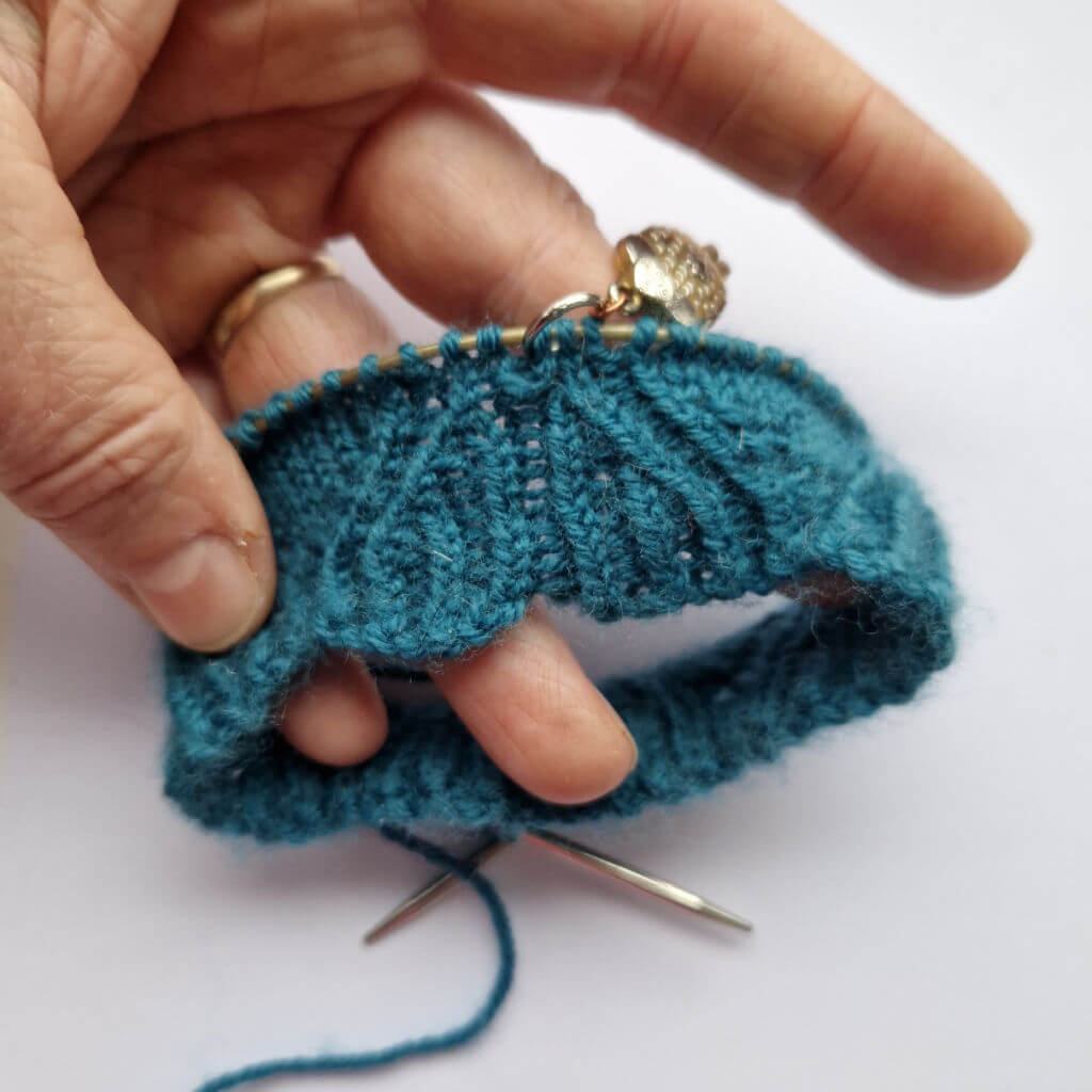 A close up of the stitch definition of a partly-knitted teal coloured sock 