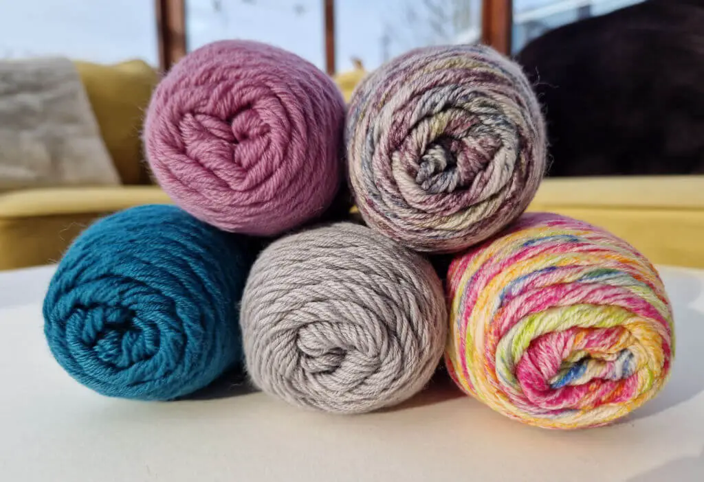 Five balls of coloured sock yarn balanced on each other on a white table.