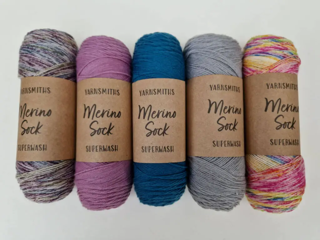 Five balls of coloured sock yarn lined up next to each other on a white background