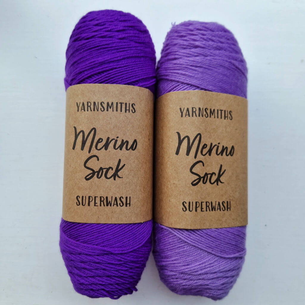 Two balls of sock yarn in dark purple and a lighter purple together on a white background