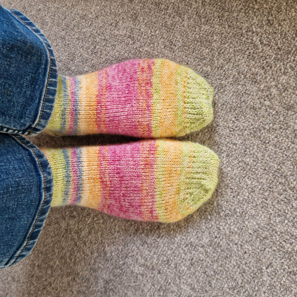 Christine is wearing a new pair of socks in stripes of pink, yellow, green and blue. She's wearing her jeans and standing on a grey carpet