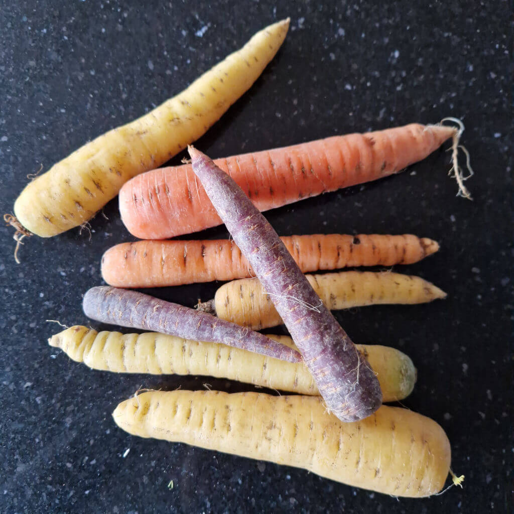 A selection of coloured carrots on a black granite worktop - they are yellow, orange and purple