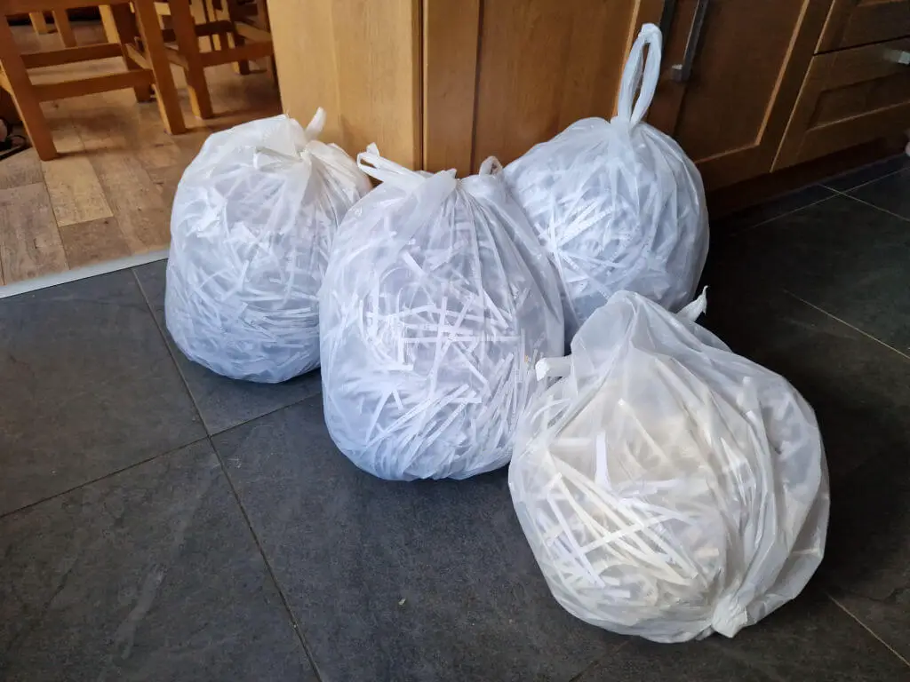 Four white bin bags on a grey tiled kitchen floor filled with shredded paper