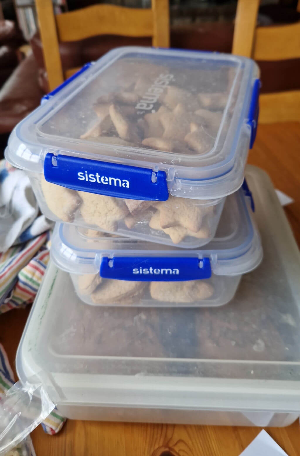 A stack of three plastic transparent storage boxes containing biscuits (cookies) sitting on a wooden table
