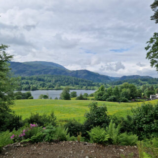 A view across Coniston water to the hills beyond. There is an abundance of green in the fields and the trees