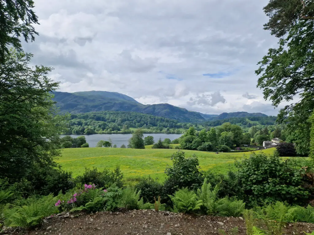 A view across Coniston water to the hills beyond. There is an abundance of green in the fields and the trees
