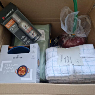 A cardboard box containing ceramic dishes, tea towels and insect repellent