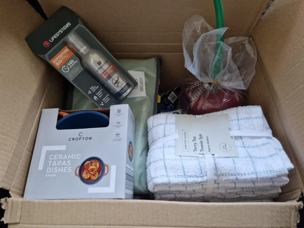 A cardboard box containing ceramic dishes, tea towels and insect repellent