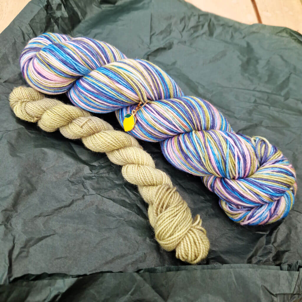 A large skein of blue and multi-coloured yarn and a smaller skein of pale green yarn on tissue paper