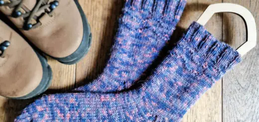 A pair blue variegated socks on sock blockers lying on a wooden floor next to a pair of hiking boots