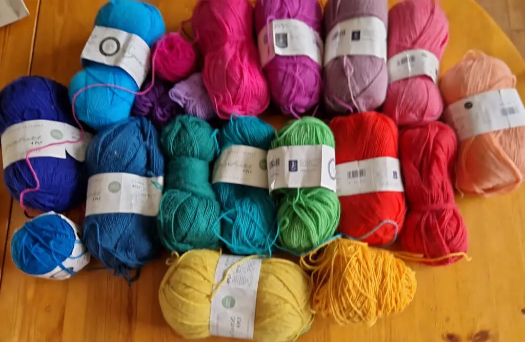 A selection of yarns in rainbow shades lying on a wooden table