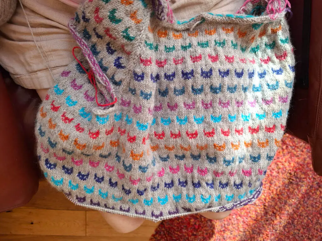 An overhead view of a grey party-knitted jumper with coloured colourwork cats
