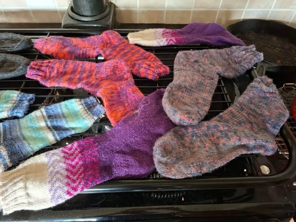 Multi-coloured pairs of hand knitted socks drying on a rack above Aga lids