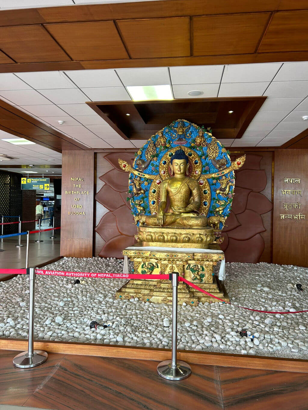 A golden Buddha statue displayed on a area filled with white stones in an airport