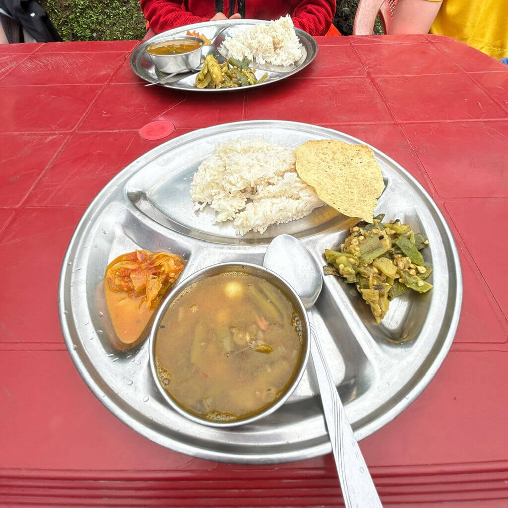 A segmented metal dish with different foods in each segment on a red table