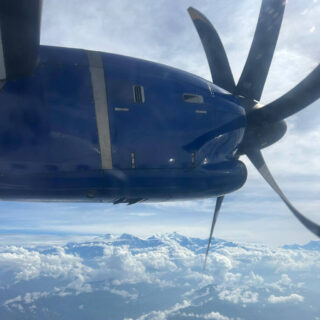 A view from an aeroplane window showing the propeller and clouds and mountains far below