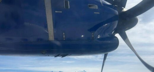 A view from an aeroplane window showing the propeller and clouds and mountains far below