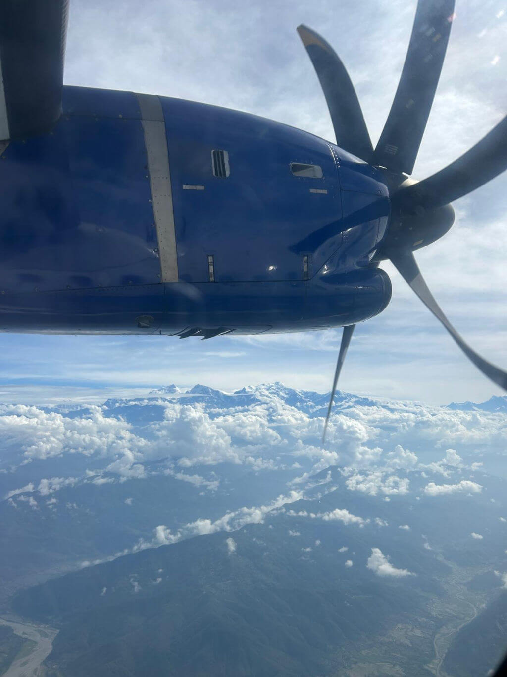 A view from an aeroplane window showing the propeller and clouds and mountains far below