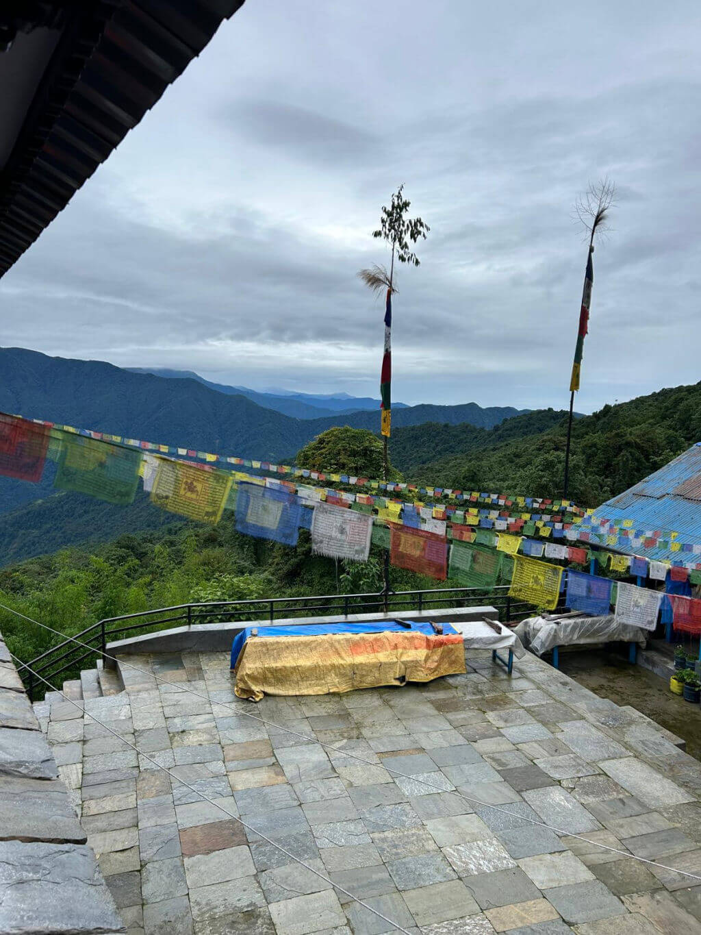 A view from a window down to a paved area with prayer flags strung across the space, and mountains in the background