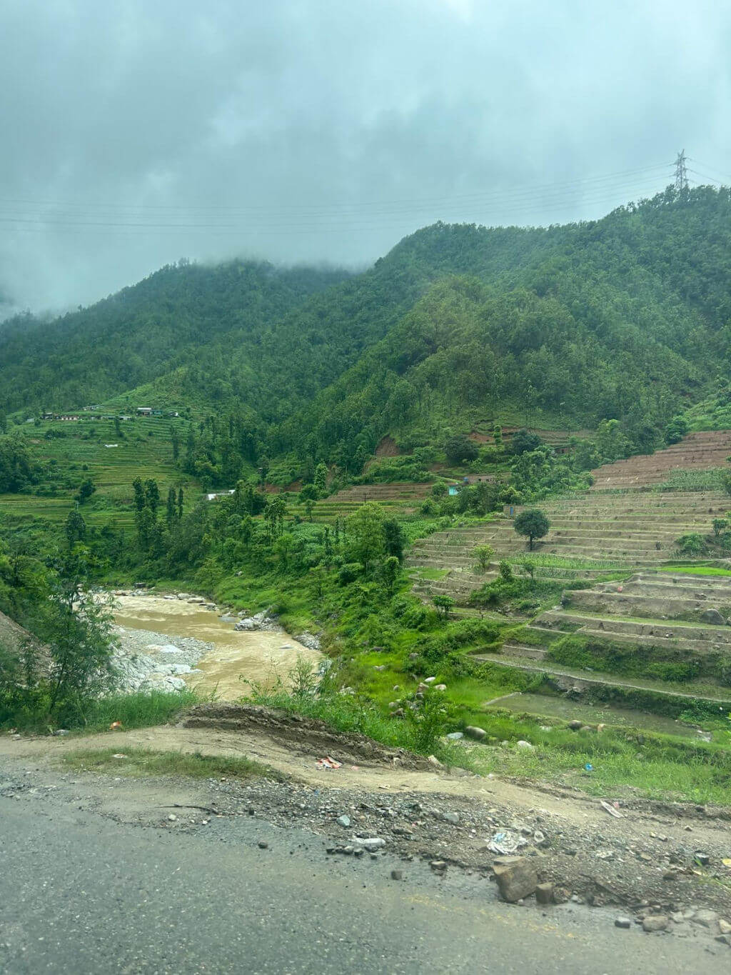 A river running at the base of terraced slopes with green tree-covered mountains in the background