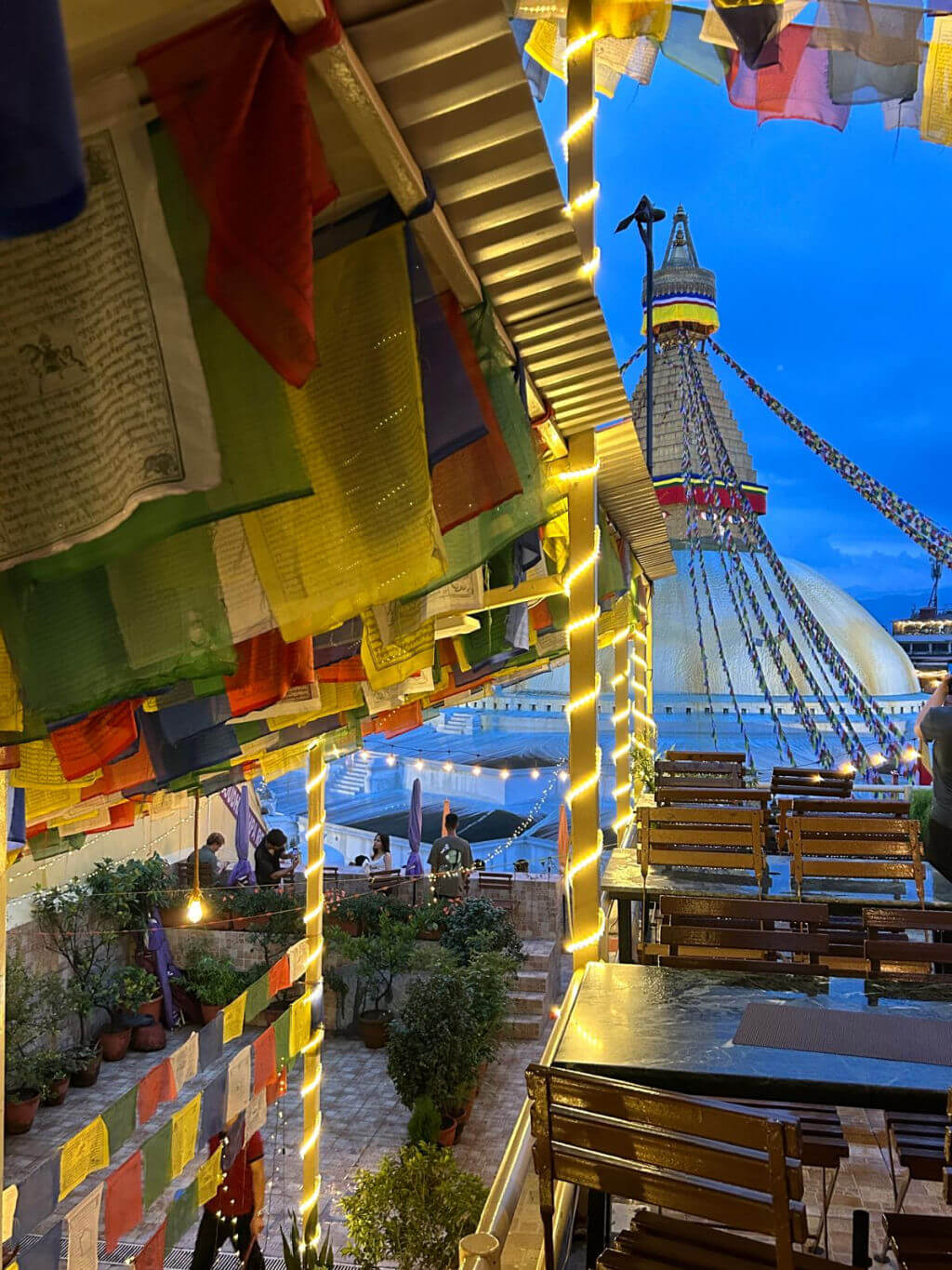 A view from a restaurant situated above the monkey temple in Nepal. There are brightly coloured prayer flags and wooden chairs and tables