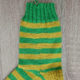 A green and yellow striped hand knitted sock on a wooden table