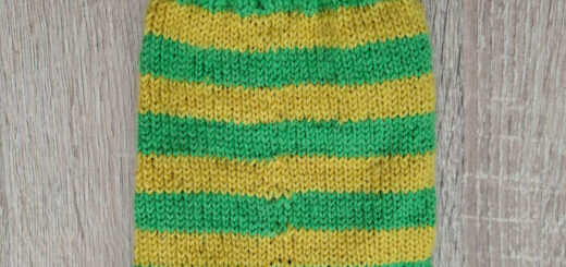 A green and yellow striped hand knitted sock on a wooden table
