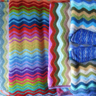 Four Attic24 Neat Ripple blankets arranged to show off the stripes, with Lucy standing on one of the blankets wearing a pair of Winwick Mum Neat Ripple socks in blue striped yarn
