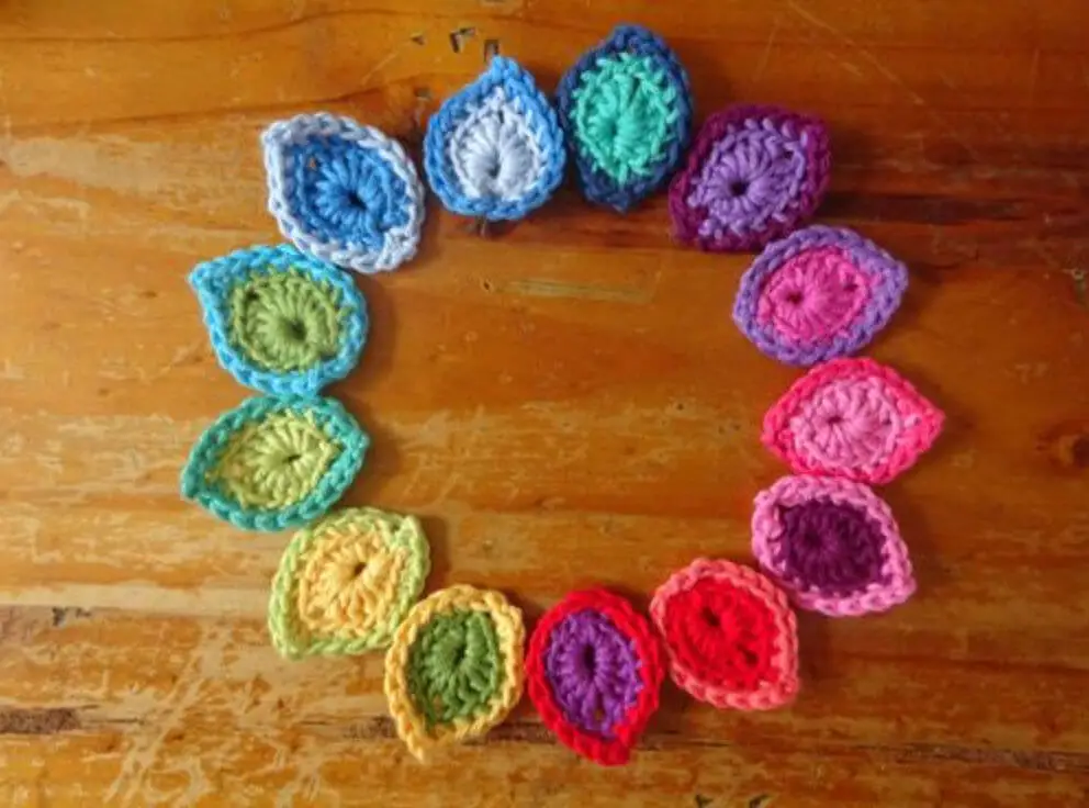 A circle of rainbow-coloured crochet leaves on a wooden table
