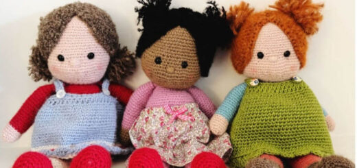 Three crocheted dolls sitting next to each other. Two have crocheted pinafore dresses, one has a fabric skirt