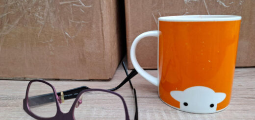 A orange mug with a sheep's face on it next to a pair of glasses