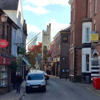 A square asymmetrical tower at the end of a narrow street of shops